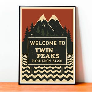 Könnte beinhalten: Ein gerahmtes Poster mit einem Vintage-Reise-Design. Das Poster zeigt ein Schild mit der Aufschrift "WELCOME TO TWIN PEAKS" mit einer Einwohnerzahl von 51.201. Der Hintergrund umfasst Berge, Bäume und einen roten Himmel.