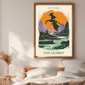 May include: A vintage-style poster for "The Hobbit" by J.R.R. Tolkien. The poster features a silhouette of a dragon flying over a landscape with mountains, a river, and a forest. The text "THE HOBBIT" is printed in bold, black letters at the bottom of the poster.