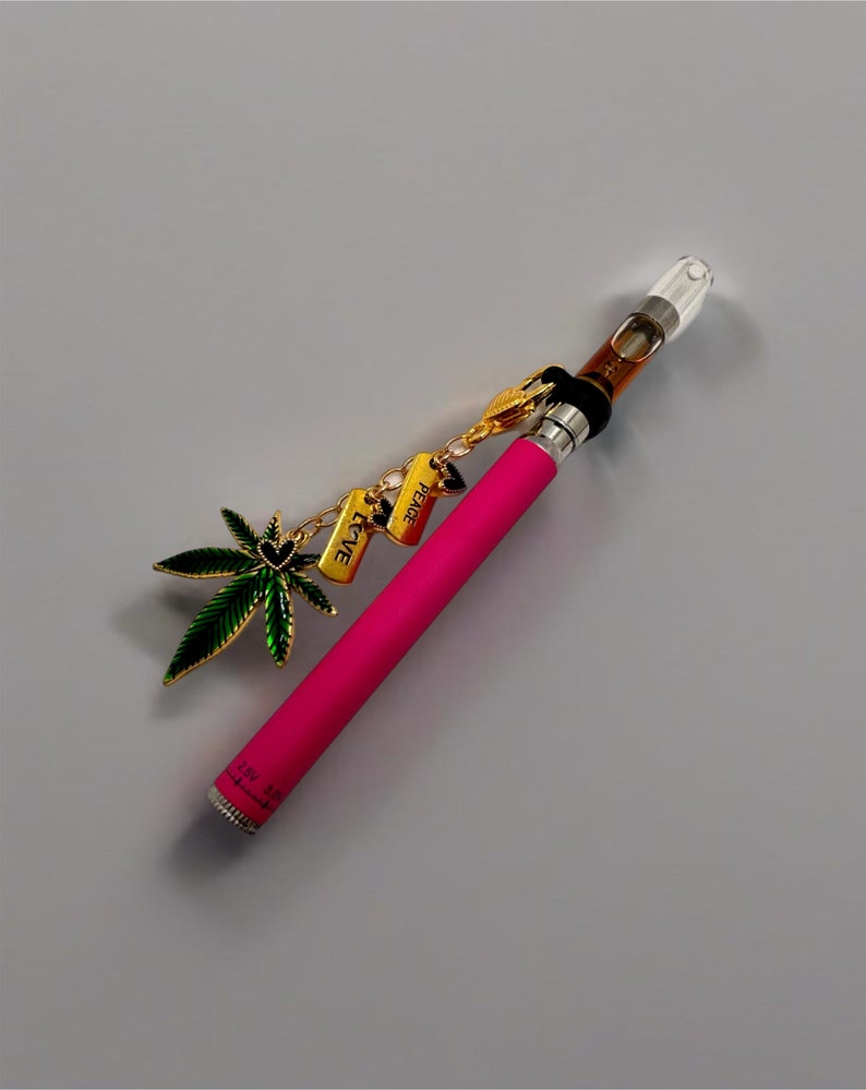May include: A pink vape pen with a clear glass mouthpiece and a gold chain with charms that say "Peace", "Love", and a green marijuana leaf.