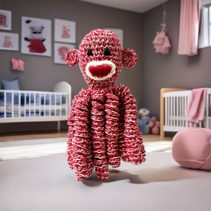 May include: A red and white crocheted octopus toy with a monkey face. The toy has a red mouth, black eyes, and a white nose.