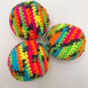 May include: Three colorful crocheted balls with a multi-colored striped pattern. The balls are made with a variety of bright colors, including pink, orange, yellow, green, blue, and black.