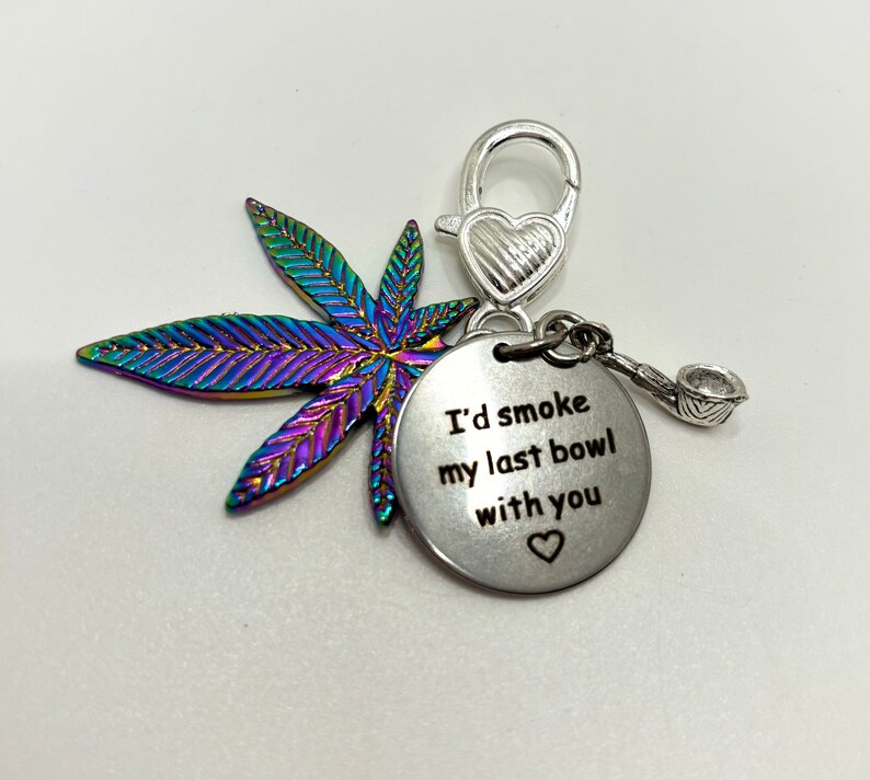 May include: A silver charm featuring a rainbow iridescent marijuana leaf, a silver heart charm, and a silver charm with the text "I'd smoke my last bowl with you" and a small heart.