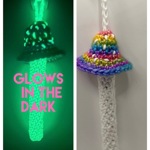 May include: A crocheted mushroom keychain with a rainbow colored top and a white stem. The mushroom glows in the dark. "Glows in the dark" is written on the image.