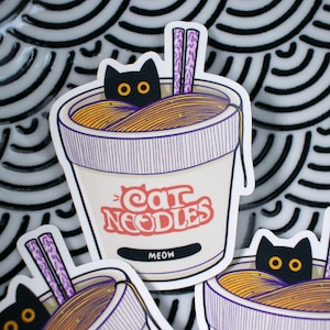 Könnte beinhalten: Ein Aufkleber mit einer schwarzen Katze in einer Schüssel mit Ramen-Nudeln. Die Schüssel ist weiß mit lila Streifen und trägt den Schriftzug "Cat Noodles Meow".