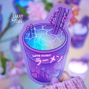 Könnte beinhalten: Ein lilafarbener Aufkleber mit einer Cartoon-Illustration einer Ramen-Schüssel, gefüllt mit blauem Wasser und einer Schwimmbadleiter. Die Schüssel hat ein neonpinkes Schild mit der Aufschrift "Late Night Ramen".