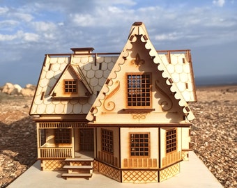 May include: A wooden model of a house with a gabled roof, intricate details, and a porch. The house is painted in a light brown color and has a white base.