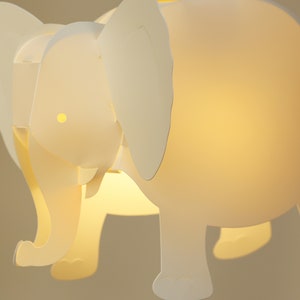 Może przedstawiać: Biała lampa w kształcie słonia ze światłem świecącym przez korpus. Lampa ma prosty design z dużymi uszami i zaokrąglonym korpusem.