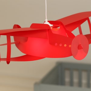 May include: A red airplane-shaped ceiling light fitting with a white cord.