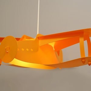 Op de afbeelding: Oranje plafondlamp in de vorm van een vliegtuig. Het licht is aan en verlicht de binnenkant van het vliegtuig.