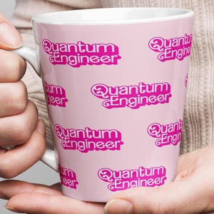 May include: A pink ceramic mug with a white handle. The mug has a repeating pattern of the words "Quantum Engineer" in pink.