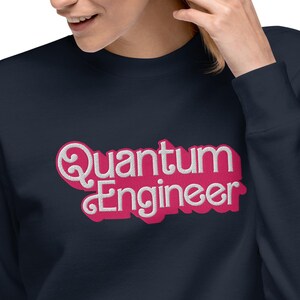 Könnte beinhalten: Ein marineblauer Pullover mit einer pinkfarbenen Grafik im Retro-Stil, auf dem "Quantum Engineer" steht.