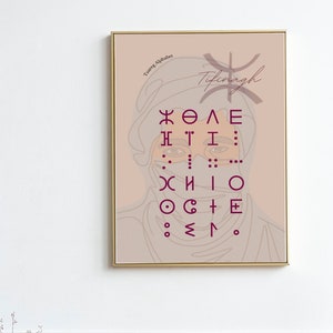 May include: A framed print with a light pink background and a gold frame. The print features a line drawing of a person's face with a veil. The text "Tifinagh" and "Tuareg Alphabet" are printed in a dark pink color at the top of the print. The print also features a series of symbols in a dark pink color.