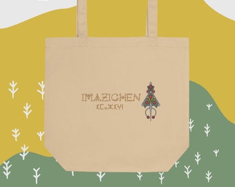 May include: A beige tote bag with a design featuring the text "IMAZIGHEN" and a stylized tree with red and green accents. The bag has two long handles.