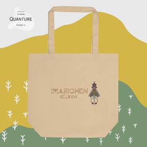 May include: A beige tote bag with a design featuring the text "IMAZIGHEN" and a stylized tree with red and green accents. The bag has two long handles.