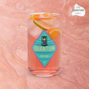 Può includere: Un bicchiere trasparente pieno di una bevanda rosa, cubetti di ghiaccio e fette di agrumi. Il bicchiere presenta un'etichetta a forma di diamante turchese e blu con il testo "QUANTUM DRINK" e "SINCE 2023". Sfondo rosa strutturato.