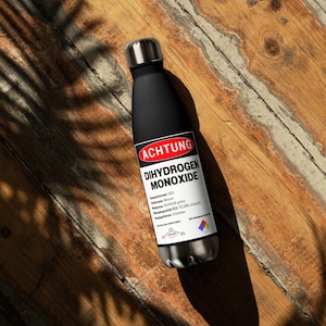 Könnte beinhalten: Eine schwarze Edelstahl-Wasserflasche mit einem Warnhinweis, der "ACHTUNG DIHYDROGEN MONOXIDE" lautet und die chemische Formel H2O enthält. Das Etikett enthält auch das deutsche Wort "Wasser", was Wasser bedeutet.