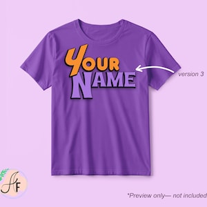Op de afbeelding: Een paars t-shirt met korte mouwen en de tekst "YOUR NAME" in een gestileerd oranje en lichtpaars lettertype. Een witte pijl wijst naar de tekst met het label "version 3" ernaast, en de tekst "*Preview only&mdash;not included" staat onderaan.