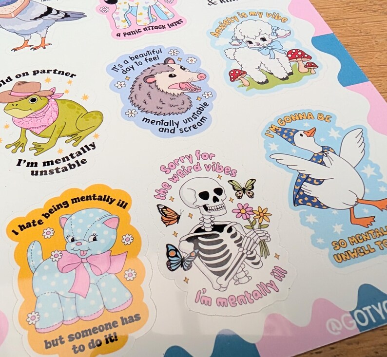 May include: A sticker sheet featuring various illustrated characters including a frog in a cowboy hat, an opossum, a lamb, a goose in a wizard hat, a blue polka-dot cat, and a skeleton holding flowers, all accompanied by humorous text.