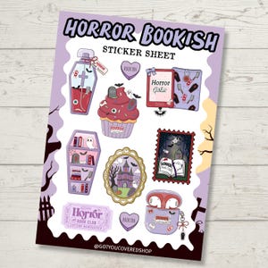 May include: A sticker sheet titled HORROR BOOKISH STICKER SHEET featuring various illustrations including a coffin-shaped bottle, a cupcake, a book, a bookshelf, a haunted house in a frame, a ticket, and a case for wireless earbuds with horror themes.
