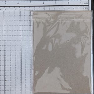 Peut inclure: Un morceau de carton rectangulaire marron enferm&eacute; dans une pochette en plastique transparent. L'objet est plac&eacute; sur un tapis de d&eacute;coupe blanc quadrill&eacute;, mesurant environ 11,5 cm de largeur et 16,5 cm de hauteur.