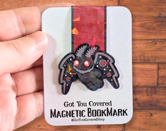 May include: A magnetic bookmark featuring a cartoon moth design with a black body, gray wings, and red accents. The bookmark has the text "Got You Covered MAGNETIC BOOKMARK" and the shop's Instagram handle.