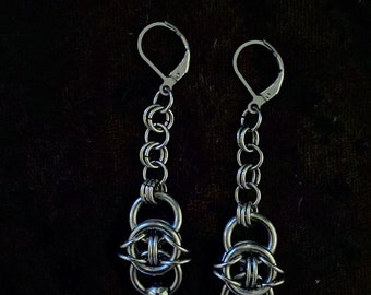 May include: A pair of silver earrings with a chain and a circular design. The earrings have a small ball at the bottom.