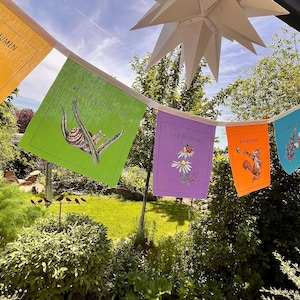 Könnte beinhalten: Eine Girlande aus bunten Gartenflaggen mit Illustrationen zum Thema Natur und deutschem Text. Die Flaggen sind in verschiedenen Farben gehalten, darunter Gelb, Grün, Lila, Orange und Blau. Die Illustrationen zeigen einen Vogel, eine Schnecke, Blumen, ein Eichhörnchen und andere natürliche Elemente.