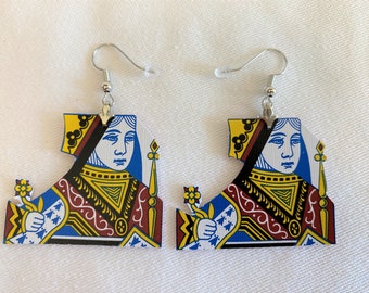 May include: A pair of earrings featuring the Queen of Spades playing card design. The earrings are made of wood and have silver hooks.