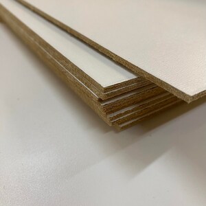 May include: A stack of white cardboard sheets with brown edges. The sheets are stacked on top of each other, with the top sheet slightly offset from the others.