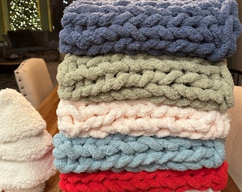Puede incluir: Una pila de seis mantas de punto grueso en varios colores, incluyendo azul, verde, rosa, azul claro, rojo y blanco. Las mantas están apiladas sobre una superficie de madera.