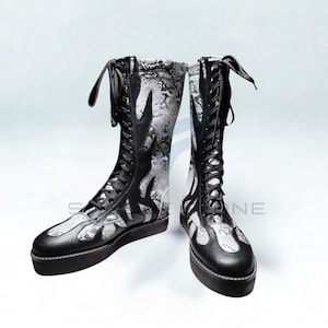 May include: A pair of black and white leather boots with a flame design. The boots have a lace-up closure and a platform sole. The upper part of the boots features a snakeskin pattern.