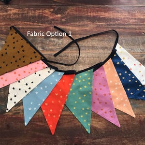 May include: A colorful fabric banner with pennant flags in various colors, including brown, pink, white, blue, red, green, purple, and orange. Each flag is decorated with small star patterns and outlined with black trim. The text "Fabric Option 1" is visible.