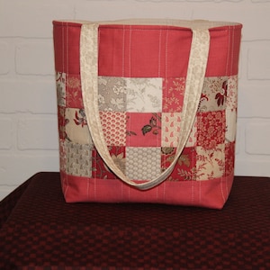 Peut inclure: Un sac fourre-tout rouge en patchwork avec des anses de couleur crème. Le sac est fait de tissu avec une variété de motifs floraux dans des tons de rouge, crème et marron.