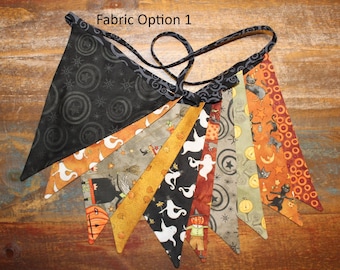 May include: A fabric bunting banner featuring multiple triangular flags with Halloween-themed patterns including ghosts, black cats, pumpkins, and stars in black, orange, green, and white. The text Fabric Option 1 is visible at the top.