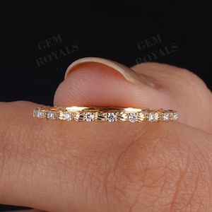 May include: A gold ring with a delicate design, featuring small, sparkling gemstones set around the band. The ring is held against a dark background, highlighting its intricate details and the brilliance of the stones.