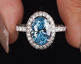 May include: A silver ring featuring a large oval blue gemstone encircled by a halo of smaller diamonds. The ring is set on a white metal band.
