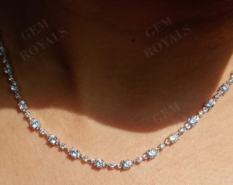 May include: A delicate silver necklace with multiple clear, round gemstones. The necklace is displayed on a person's neck, showcasing the sparkling stones. The gemstones are evenly spaced along the chain, creating a classic and elegant look.