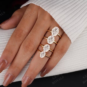 Pode incluir: Um conjunto de cinco an&eacute;is de noivado de diamantes ovais em tamanhos diferentes, engastados em bandas de ouro. Os an&eacute;is s&atilde;o exibidos em uma m&atilde;o que est&aacute; usando um su&eacute;ter branco.