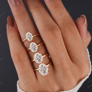 Pode incluir: Cinco an&eacute;is de ouro com diamantes de forma oval de diferentes tamanhos. Os an&eacute;is est&atilde;o empilhados em uma m&atilde;o que est&aacute; usando um su&eacute;ter branco.
