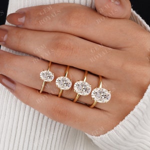 Pode incluir: Cinco an&eacute;is de ouro com diamantes de forma oval de tamanhos diferentes. Os an&eacute;is est&atilde;o na m&atilde;o de uma pessoa.