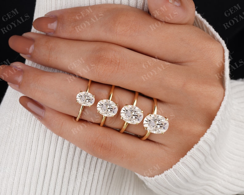 Pode incluir: Cinco an&eacute;is de ouro com diamantes de forma oval de tamanhos diferentes. Os an&eacute;is est&atilde;o na m&atilde;o de uma pessoa.