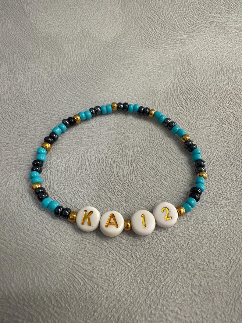 May include: A turquoise and black beaded bracelet with white beads spelling out the name "KAI2".