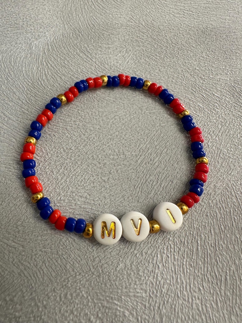 May include: A red, blue, and gold beaded bracelet with white beads that spell out the letters "MVI".