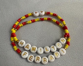 May include: A red and yellow beaded bracelet with the words "Hamilton" and "Ferrari" spelled out in gold letters on white beads.