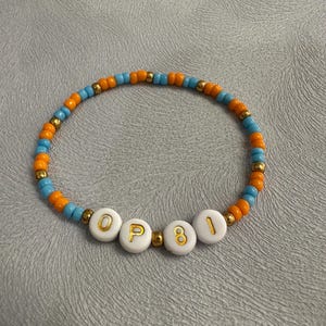 May include: A beaded bracelet with orange and blue beads and white letter beads spelling "OP81".