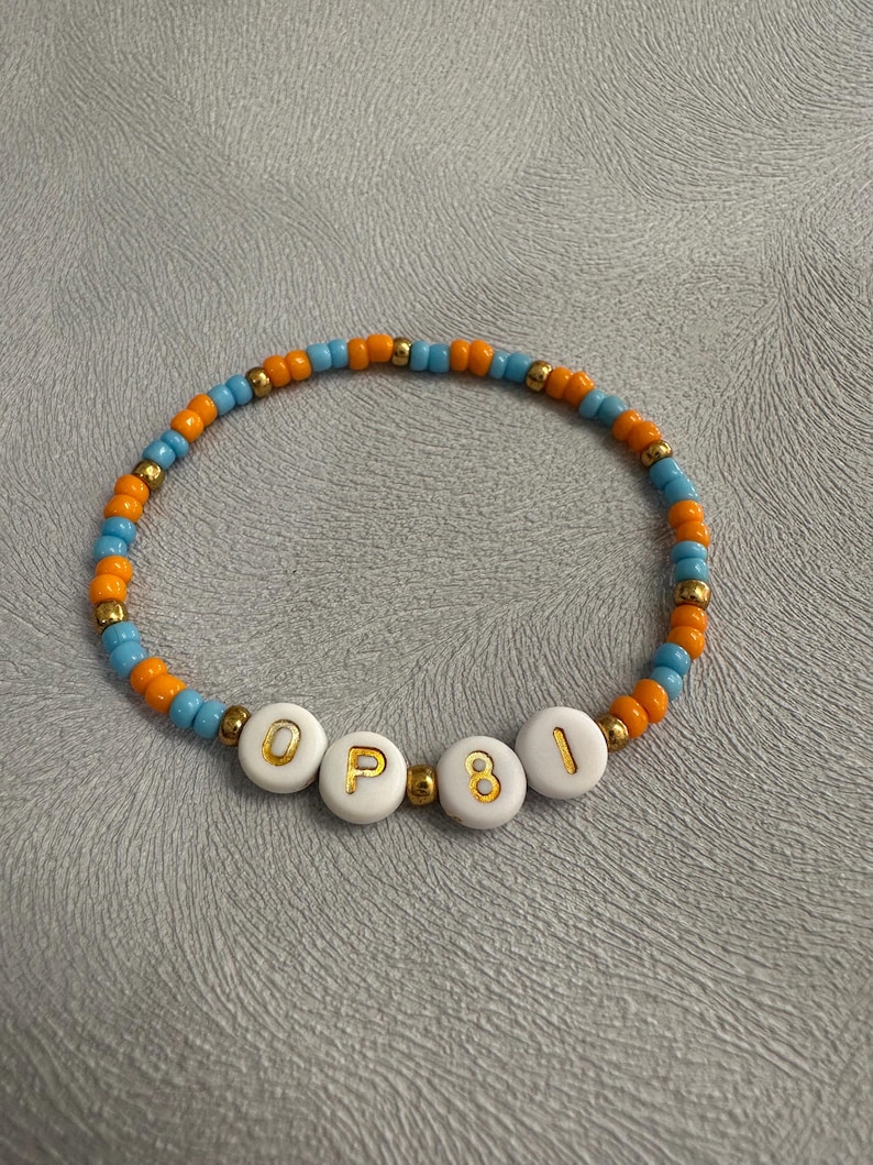 May include: A beaded bracelet with orange and blue beads and white letter beads spelling "OP81".