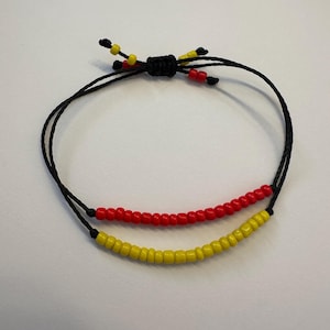 May include: A black string bracelet with red and yellow beads. The bracelet is tied with a knot at the top.