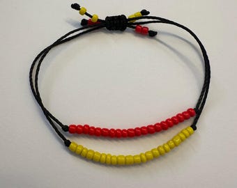 May include: A black string bracelet with red and yellow beads. The bracelet is tied with a knot at the top.