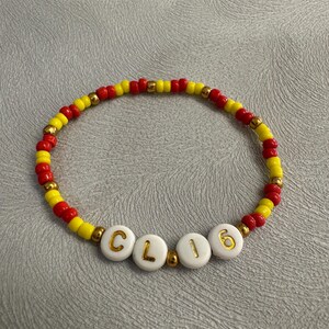 May include: A red and yellow beaded bracelet with the word "CL16" spelled out in gold letters on white beads.