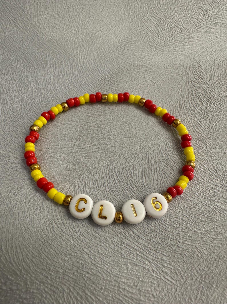 May include: A red and yellow beaded bracelet with the word "CL16" spelled out in gold letters on white beads.